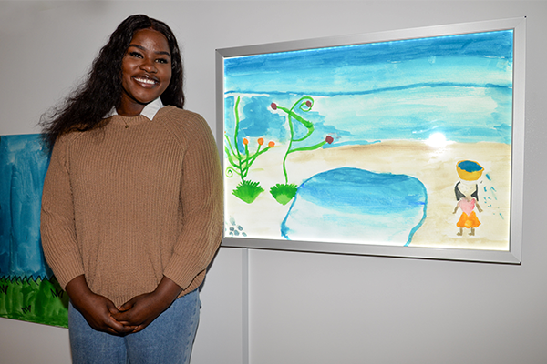Katty Okeny stands in front of her artwork