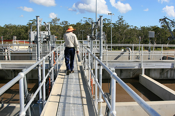 A council worker at a water treatment plant walking on a narrow bridge